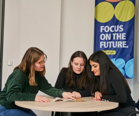 drei Frauen sitzen an einem Tisch und schauen eine Brosch&uuml;re an