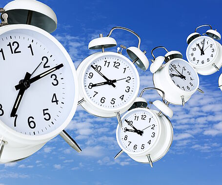 Wecker mit verschiedenen Uhrzeiten, die durch einen blauen Himmel fliegen