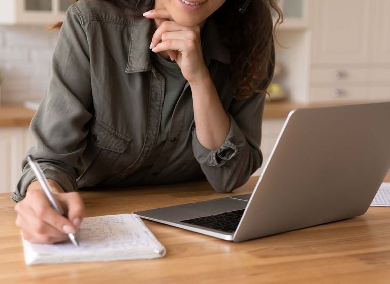 Smiling young female remote student watch laptop lecture take notes