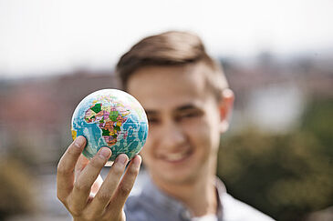 ein kleiner Globus wird von einer m&auml;nnlichen Person in der rechten Hand hochgehalten