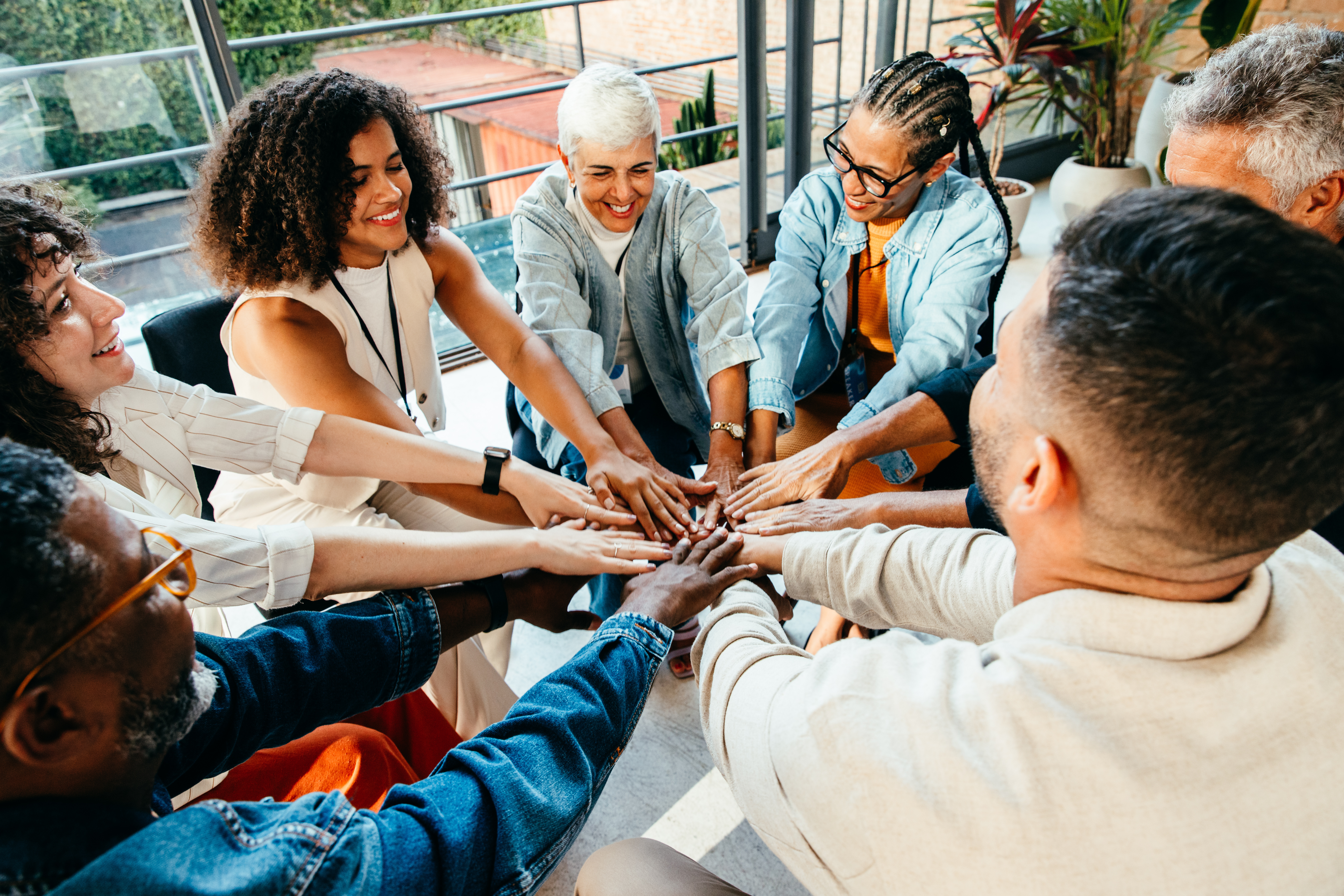 Diverse group of people coming together, placing h Diverse group of people coming together, placing hands in unity during a team building session in a modern office setting.
