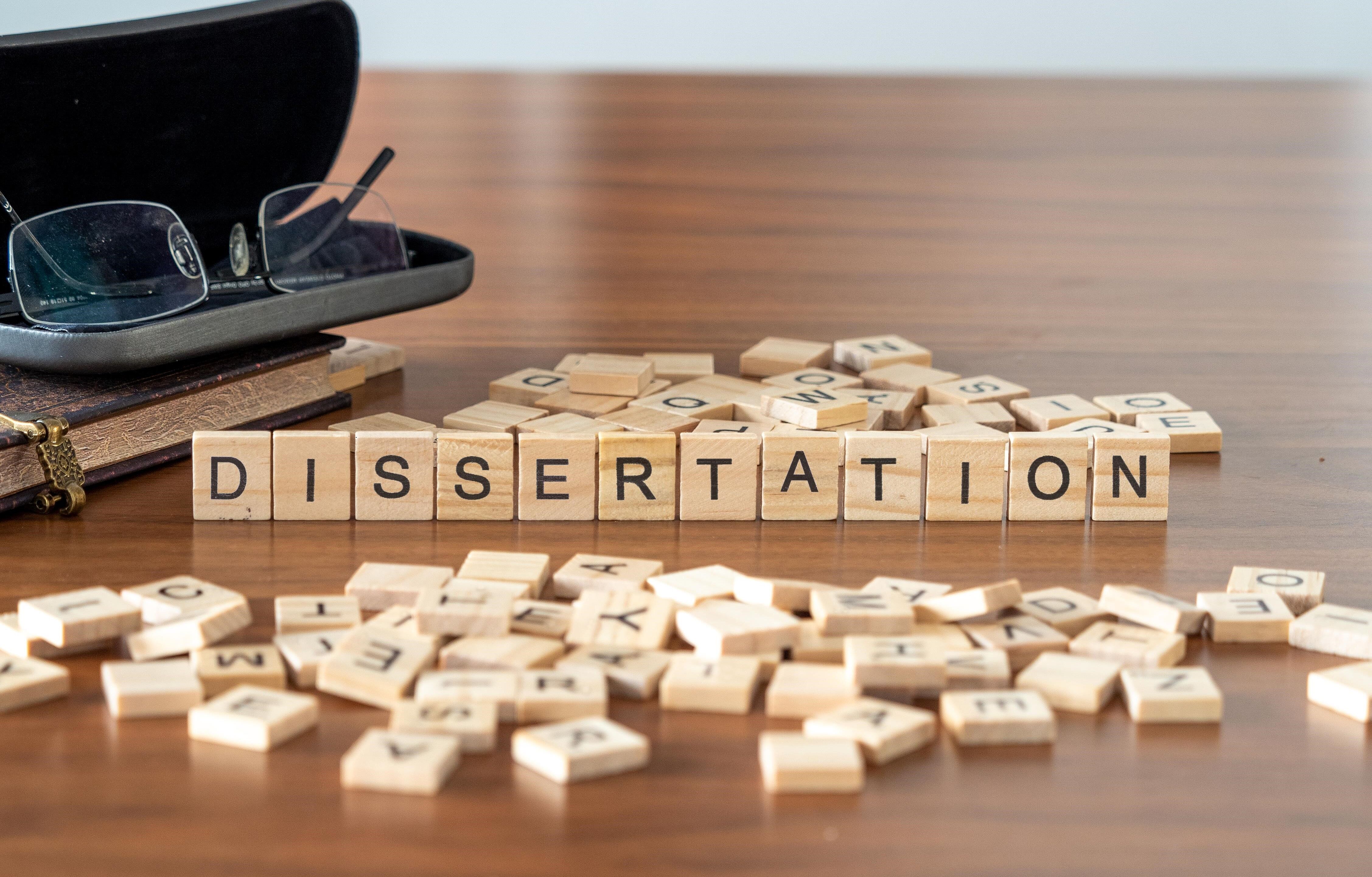 dissertation word or concept represented by wooden letter tiles on a wooden table with glasses and a book
