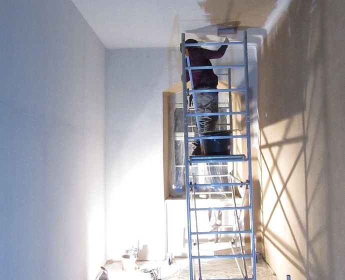 Das Bild zeigt das Musterzimmer während der Bauphase. Man sieht eine Leiter auf der ein Studierender steht und die Zimmerdecke streicht.