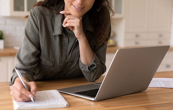 Smiling young female remote student watch laptop lecture take notes