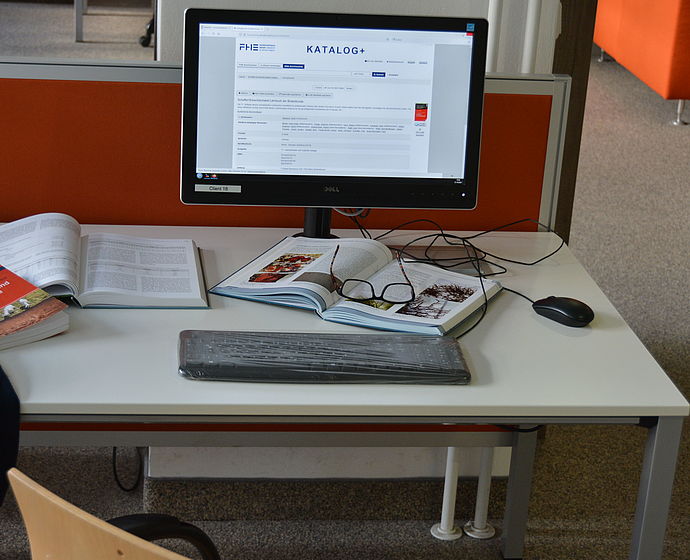 Arbeitsplatz mit Bildschirm, Tastatur, Maus, aufgeschlagenen Büchern