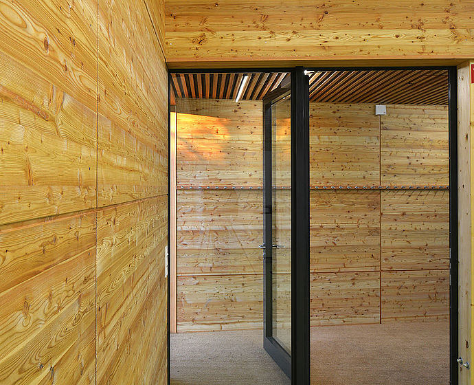 Blick vom Innenraum mit grünem Fußboden und natürlichen Holzwänden auf den Vorflur.