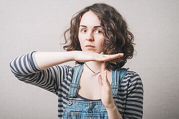 The woman has her hands stop timeout. On a gray background.