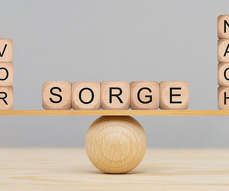 Darstellung einer ausbalancierten Wippe mit drei Holzwürfeln auf der linken Seiten, dies das Wort Vor ergeben, vier Holzwürfeln auf der rechten Seite, die das Wort Nach ergeben und in der Mitte fünf Würfeln, dies das Wort Sorge ergeben. Vorsorge ist besser als Nachsorge