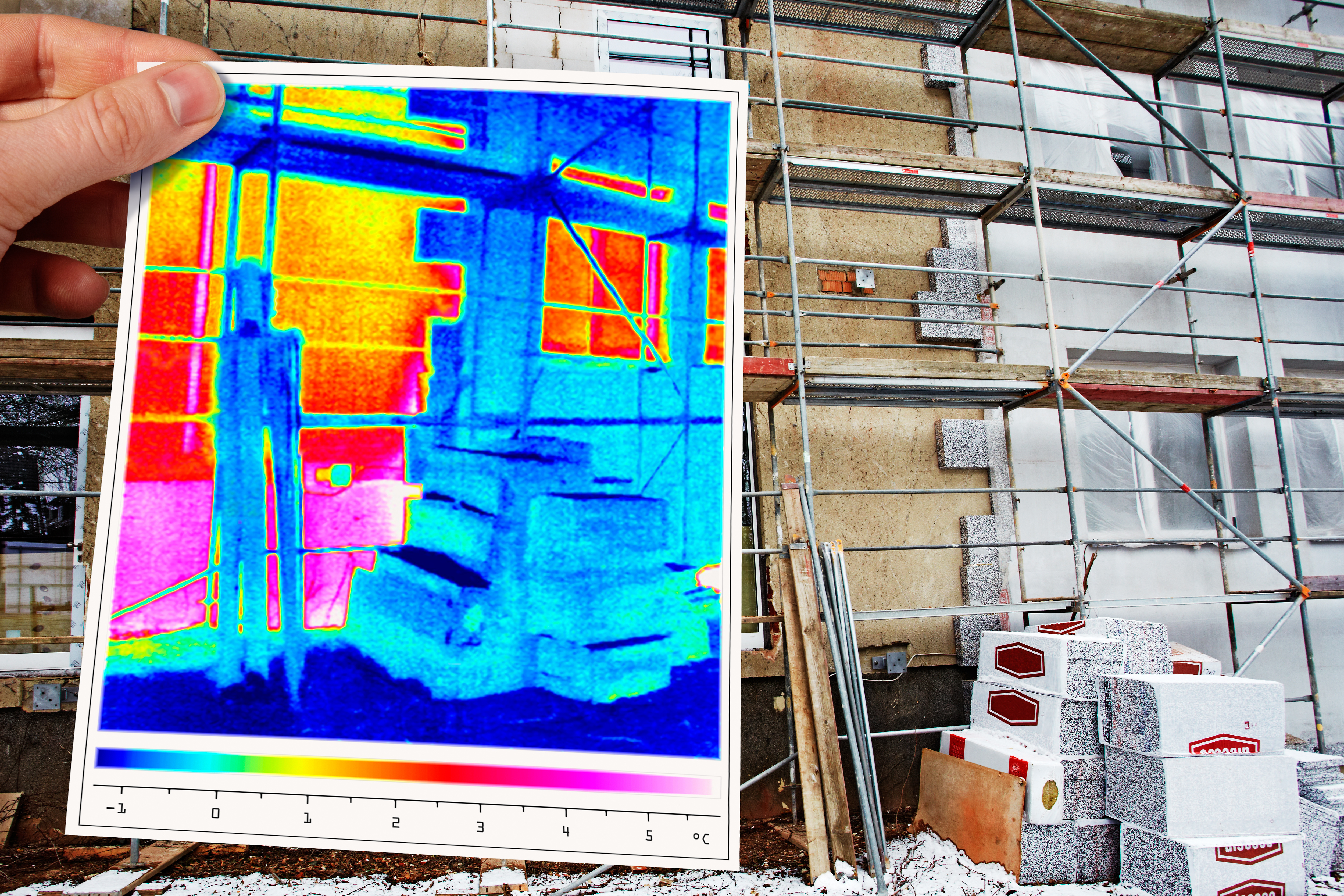 Thermografieaufnahme, die mit der Hand vor einer sanierte Gebäudefassade gehalten wird